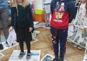 Na zdjęciu widać dwoje dzieci, chłopca i dziewczynkę, które stoją na gazecie