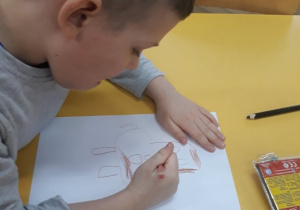 Na zdjęciu widać chłopca siedzącego przy stoliku, który rysuje coś na kartonie