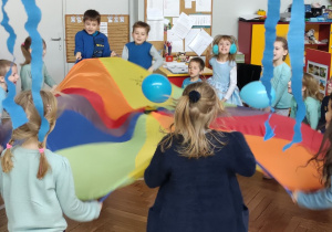 Zdjęcie przedstawia dzieci podrzucające na chuście animacyjnej niebieskie balony.