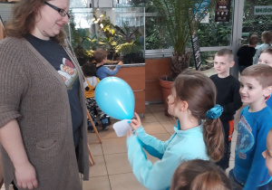 Zdjęcie przedstawia dzieci wręczające kobiecie niebieski balonik.