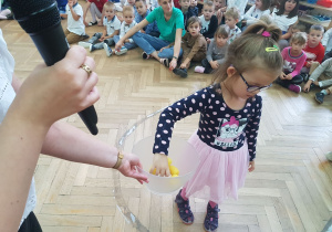 Zdjęcie przedstawia dziewczynkę losującą z miski żółte jajko z pytaniem.