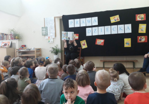 Zdjęcie przedstawia zgromadzone dzieci przed Panią Agatą, które słuchają czytanego opowiadania z książki " Mały obywatel świata"