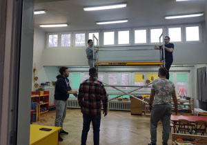 na zdjęciu widać salę przedszkolną, trzech mężczyzn stoi na podłodze dwóch na rusztowaniu