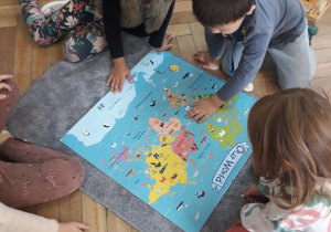 Zdjęcie przedstawia dzieci pracujące z mapą świata, która została ułożona na szarym dywaniku.